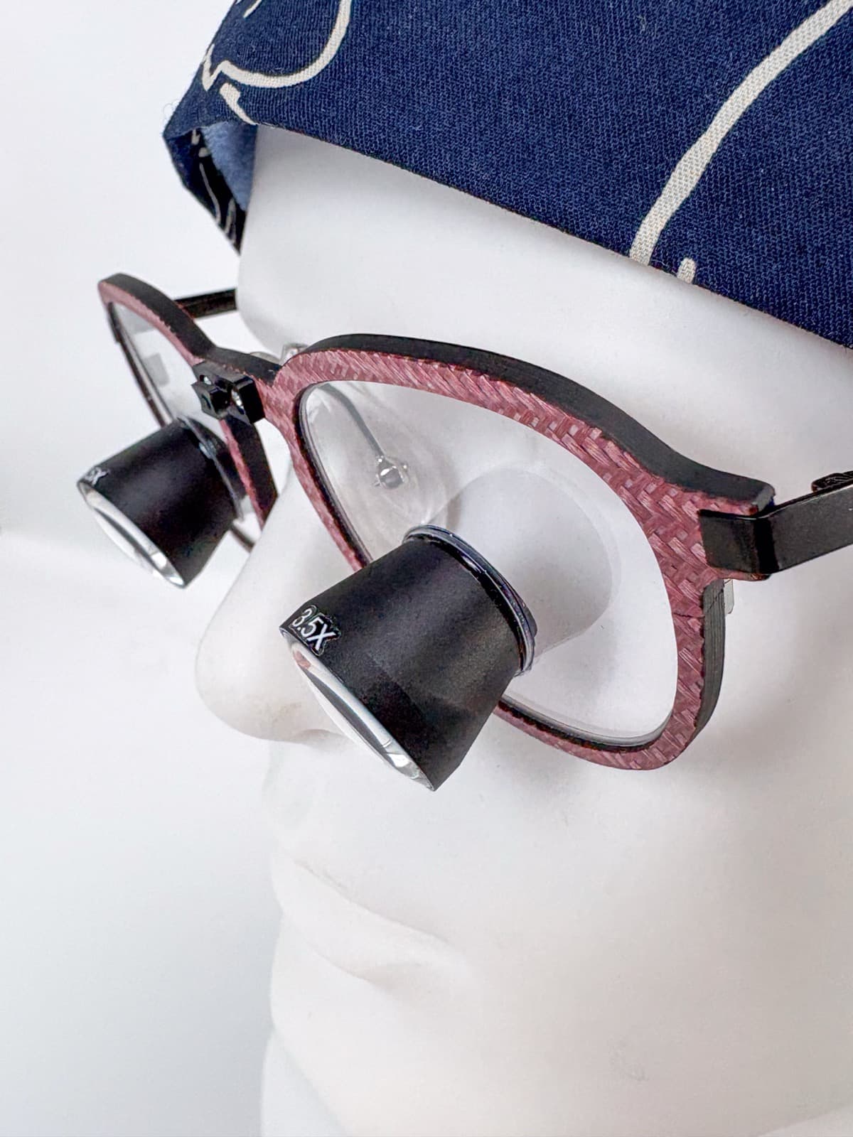 ACUVIEW crimson red carbon fiber surgical loupes on a mannequin head, 3/4 close-up